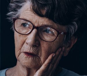 Closeup on an elderly woman's face leaning on her hand as she looks out a window, meaning to signify the isolation of substance abuse in the elderly.