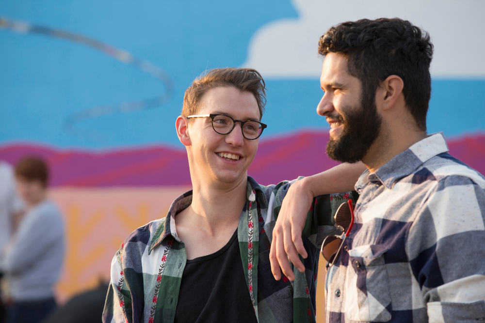 Two men talking to each other, one with his arm on the other man's shoulder, both wearing black, white and grey plaid unbuttoned flannel shirts, discussing VOASW aftercare.